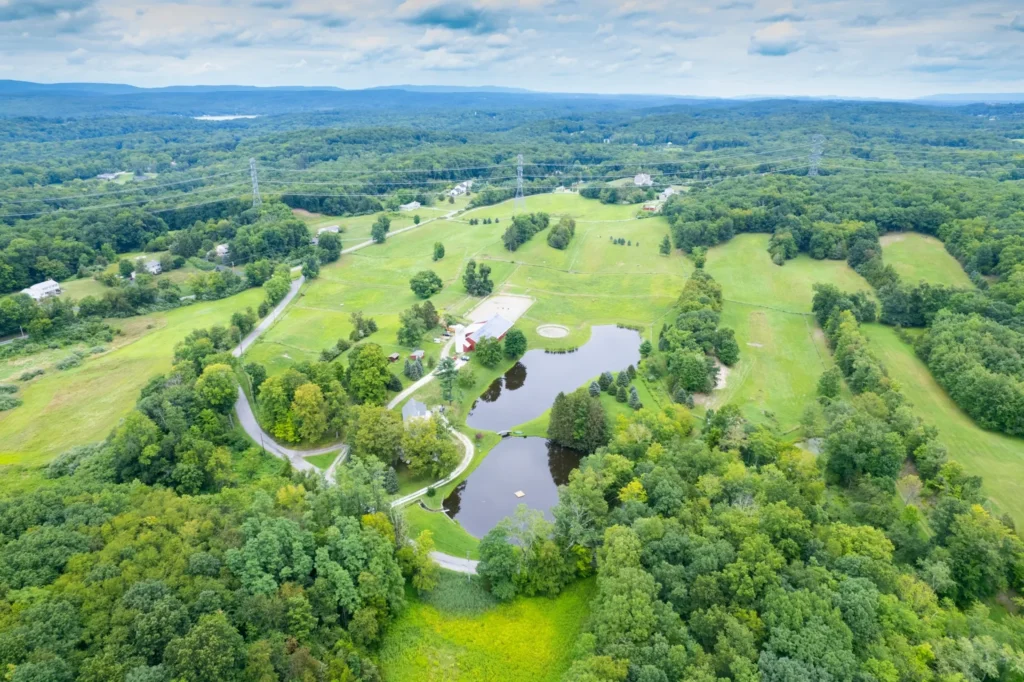 Aerial view of a preserved teaching farm surrounded by rolling fields, wooded areas, barns, and connected pond ecosystems used for agricultural education.